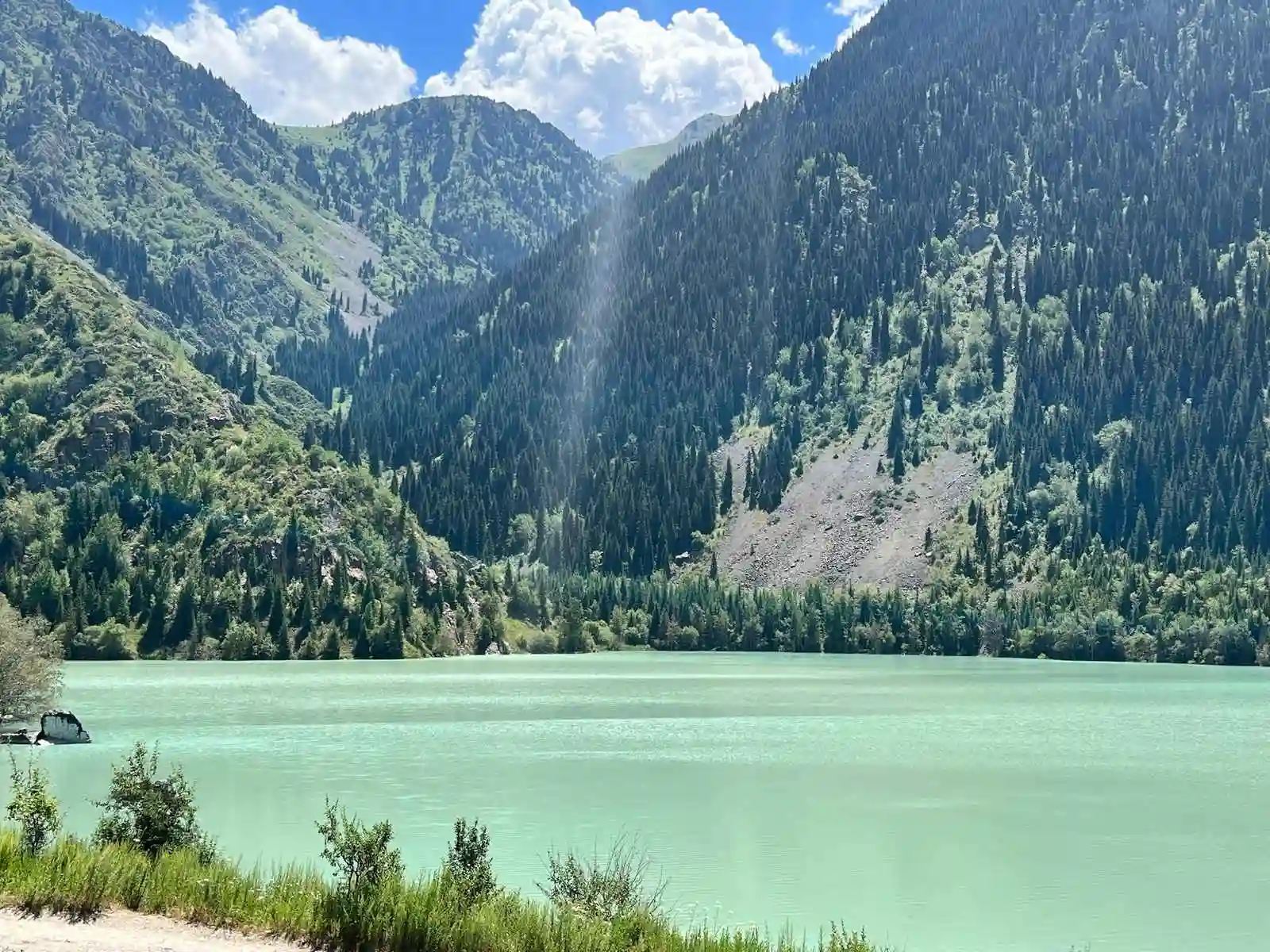 Turquoise waters of Issyk Lake surrounded by pine-covered mountains